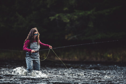 Woman angler in waders walks through rushing water in river