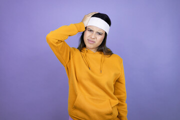 Young latin woman wearing sportswear over purple background putting one hand on her head smiling...