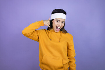 Young latin woman wearing sportswear over purple background smiling doing phone gesture with hand and fingers like talking on the telephone