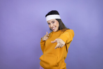 Young latin woman wearing sportswear over purple background pointing to you and the camera with fingers, smiling positive and cheerful