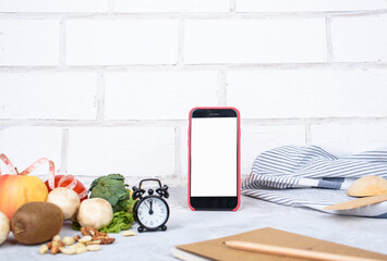 Phone with white mockup, little clock, and different kitchen and cooking utensils on light table. Culinary blog, recipe template, online cooking courses.