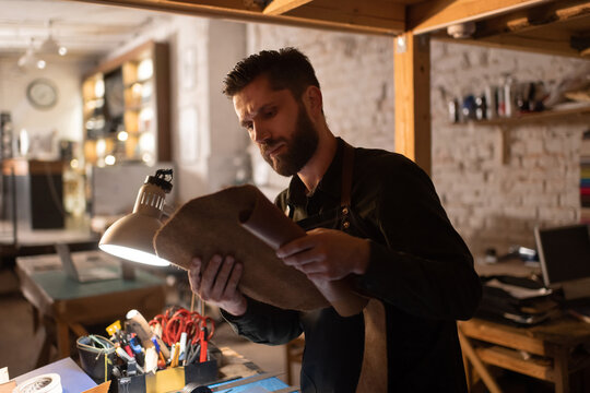Bearded craftsman examining piece of leather