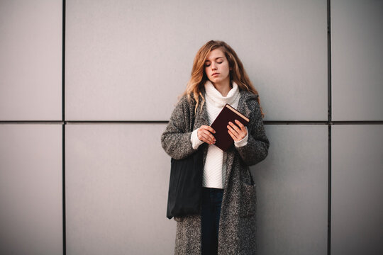 Portrait of female student holding book standing against gray wall