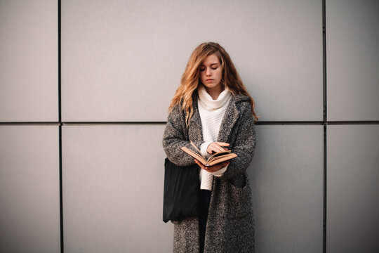 Portrait of female student holding book standing against gray wall