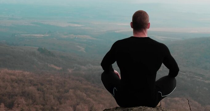 A young athletic man meditating on top of a mountain, yoga meditation exercise in nature. Breathing exercises
