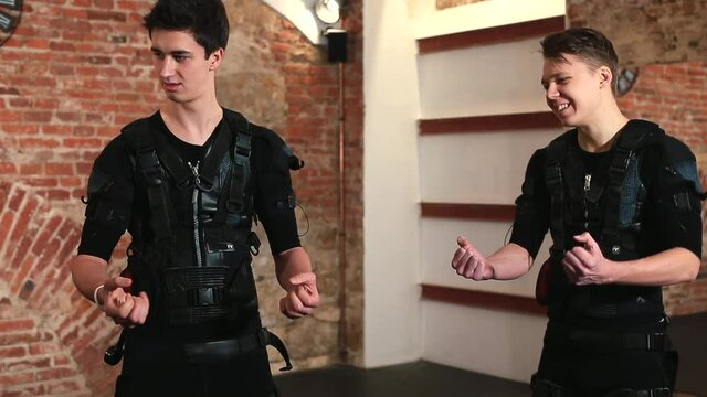 Two men in electronic vests tune the stimulation sensors. Preparing for a workout gym. He analyses the sensitivity of the current, shows and laughs.