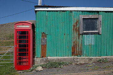 Old red telephone booth contrasting with green corrugated iron
