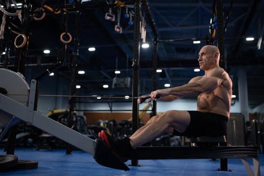 Strong senior man doing rowing exercise in modern gym
