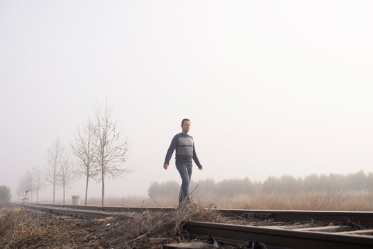 Man in dense fog are walking along the railway tracks.