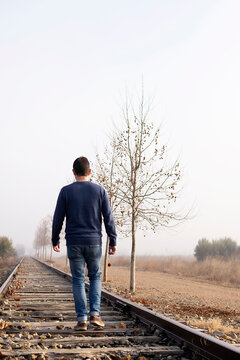 Rear view of a man walking along the railway tracks.