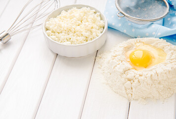 Baking cake in rustic kitchen - dough recipe ingredients eggs, flour, milk, butter, sugar on white planked wooden table from above. Background layout with free text space