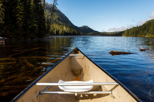 Bow of a canoe a secluded lake surrounded by forest, mountains and sky