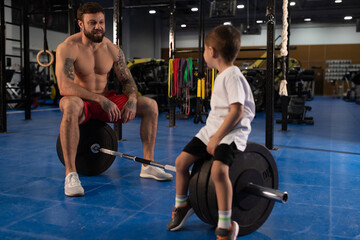 Father and son sitting on barbell during break in gym