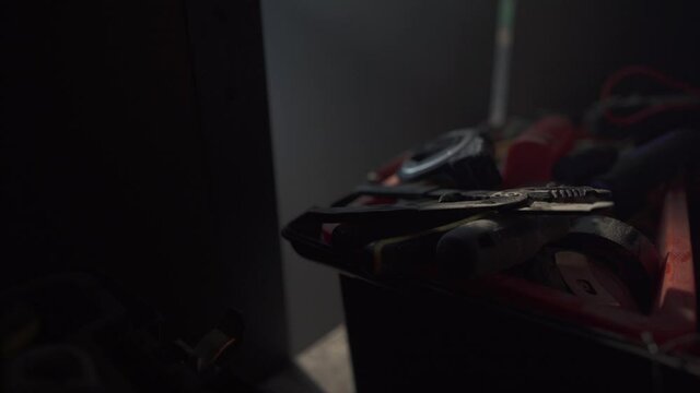 Man puts away a pair of pliers into tool box and closes cupboard doors.  Smokey dark setting.