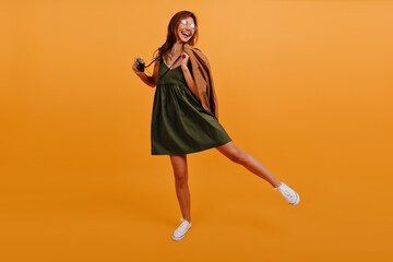 Cheerful joyful girl in summer sundress is having fun and dancing on isolated background. Photo in studio model in full growth with camera in hand