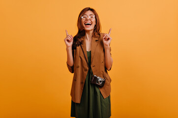 Laughing young woman in beige clothes shows fingers up after appearance of fun idea