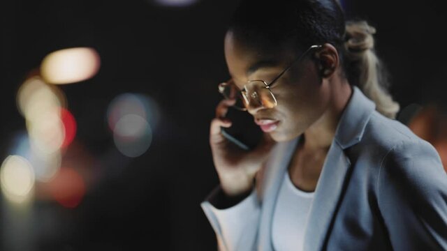 Busy beautiful afro-american businesswoman employee calling business partners with smartphone conversation talking inside corporate dark office.
