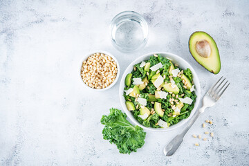 Kale avocado pine nuts cheese salad with lemon dressing in a bowl