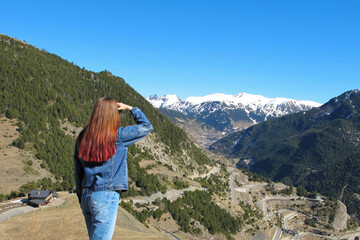 A girl with red hair looks at the mountain's landscape against the bright blue sky.  Travel content