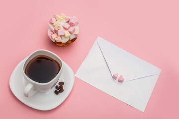 Blank envelope and White cup full of coffee with tasty cupcake with hearts from marshmallow on pink background