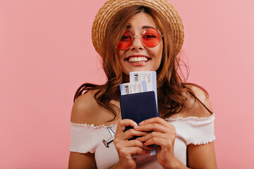 Closeup portrait of charming lady in pink glasses and straw hat with trepidation holding passport...