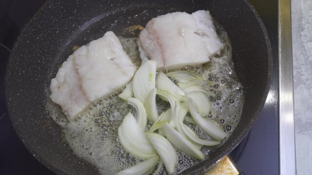 Add fresh onion to the fillet of sea cod fis is fried in a frying pan. Cooking at home