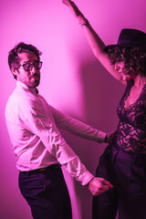 Studio lifestyle, a young Caucasian couple dancing, with neon pink light