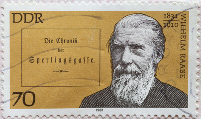 a postage stamp from Germany, GDR showing a portrait of Wilhelm Raabe (1831–1910), poet and narrator, in the background the book title The Chronicle of Sperlingsgasse . Great personalities - obrazy, fototapety, plakaty
