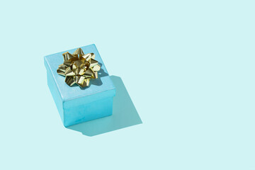 Blue gift with the golden bow on the pastel blue background birthday or other celebration