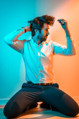 Lifestyle studio, a Caucasian man on his knees wearing a white shirt, illuminated with an orange and blue neon light