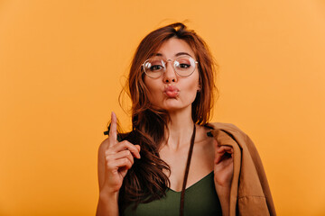 Funny attractive girl sends kiss to camera. Portrait of cute positive lady in autumn clothes on orange background