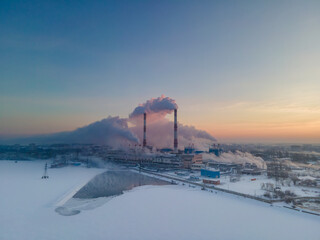 Smoke stacks over sunrise sky background at freezing weather morning with haze. Energy generation and air environment pollution industrial scene.