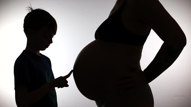 Silhouette of a teenager and a belly of a pregnant woman. He touches mom's belly. Investigation of the secret connection of energy proximity. Natural parenting.