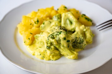 Stewed broccoli in creamy sauce with boiled potato on white plate.