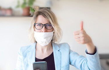 A woman in a mask and with a phone to stop viral and epidemic diseases. European blond woman in mask with hand shows like. Online consultation