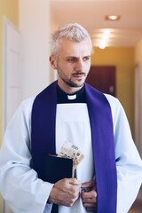 Polish catholic priest holding and counting money during pastoral visit in Poland. Tradition in...