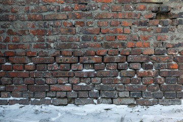 Brick background, dark ancient brick wall and part of the ground in the snow