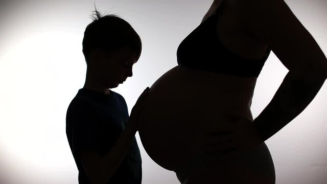 The silhouette of a son gently touches the belly of a pregnant mother. Waiting for the birth of a new family member. Experienced parenting.