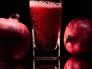 Glass in the low-key lighting with two pomegranates and juice