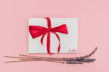 White envelope with red ribbon and red hearts isolated on pink background with dry lavender flowers