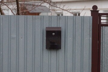 one brown mailbox hanging on a gray metal fence wall on the street