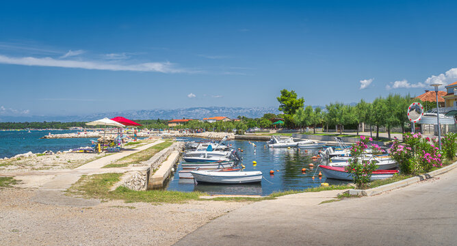 Small marina with moored motorboats in Zaton bay. Families having fun in turquoise water of Adriatic Sea with Dinaric Alps in background, Croatia