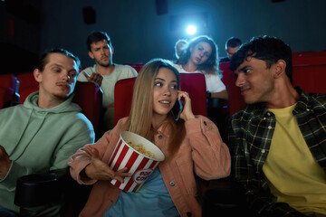 Cheerful young woman talking on the phone, annoying audience while watching movie with friends at the cinema - obrazy, fototapety, plakaty