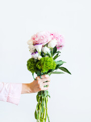 Female hand holding beautiful pastel peony bouquet on light gray background.
