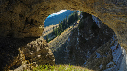 An arched cave eroded in a calcareous cliff located on top of Latorita mountains. The formation opens to a mountainous view: the grassy crests of Fratosteanu Peak. Carpathia, Romania.