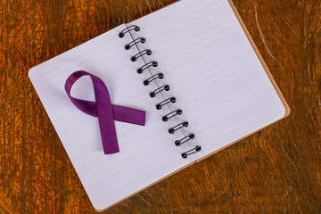 spiral notebook open on wooden table with purple ribbon bow, representing February purple, month of awareness about lupus, fibromyalgia and Alzheimer's. Space to text.