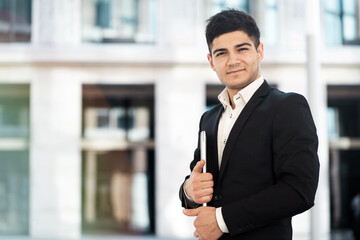 the manager is a brunette of European appearance standing in the business center in a stylish black suit. holds in his hands works on a laptop computer. copy space. banner for the site.