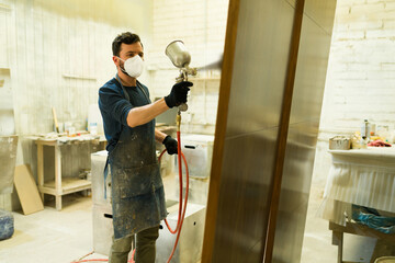 Male worker painting a brown door in a woodshop