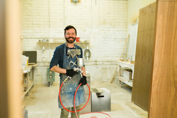 Smiling male worker using a spray gun to paint a wooden door