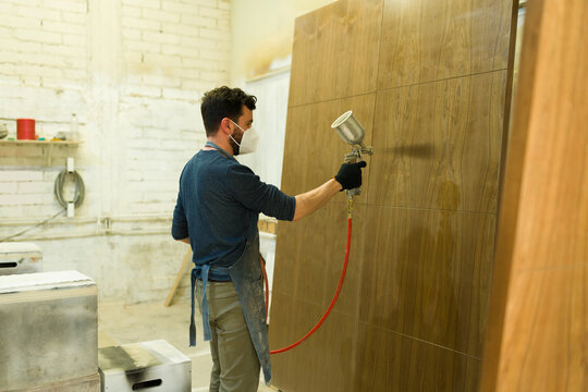 Rear view of a carpenter spraying with paint a wood door